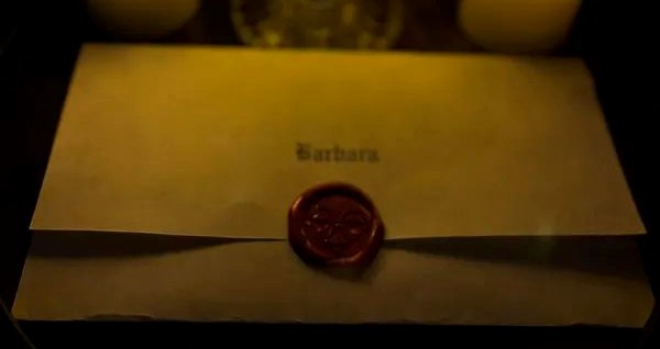 A parchment envelope addressed in blackletter and pressed with a crimson wax seal, lit by candles